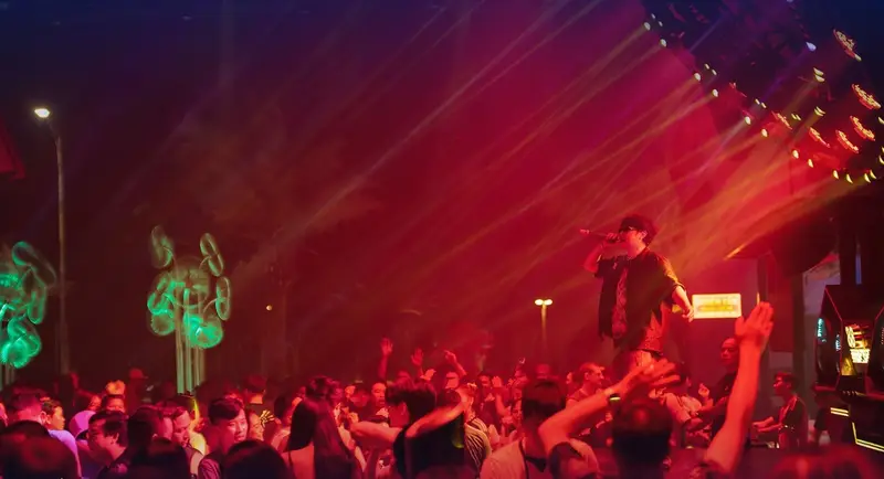 Ca sĩ khách mời trên sân khấu ngoài trời, laser đỏ quét qua hàng cọ và cây đèn neon tại 88 Beer Garden Vũng Tàu